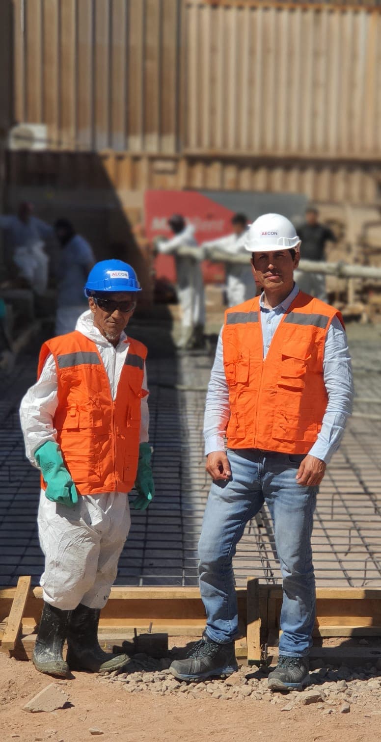 Dos trabajadores de AECON con equipo de protección junto a una malla de refuerzo para hormigón