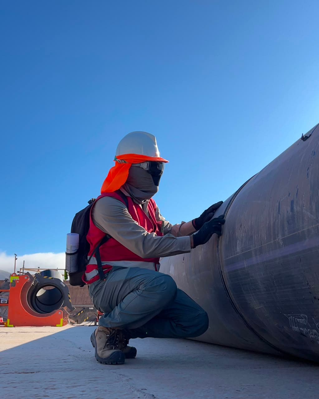 Trabajador AECON inspeccionando tubería industrial en terreno